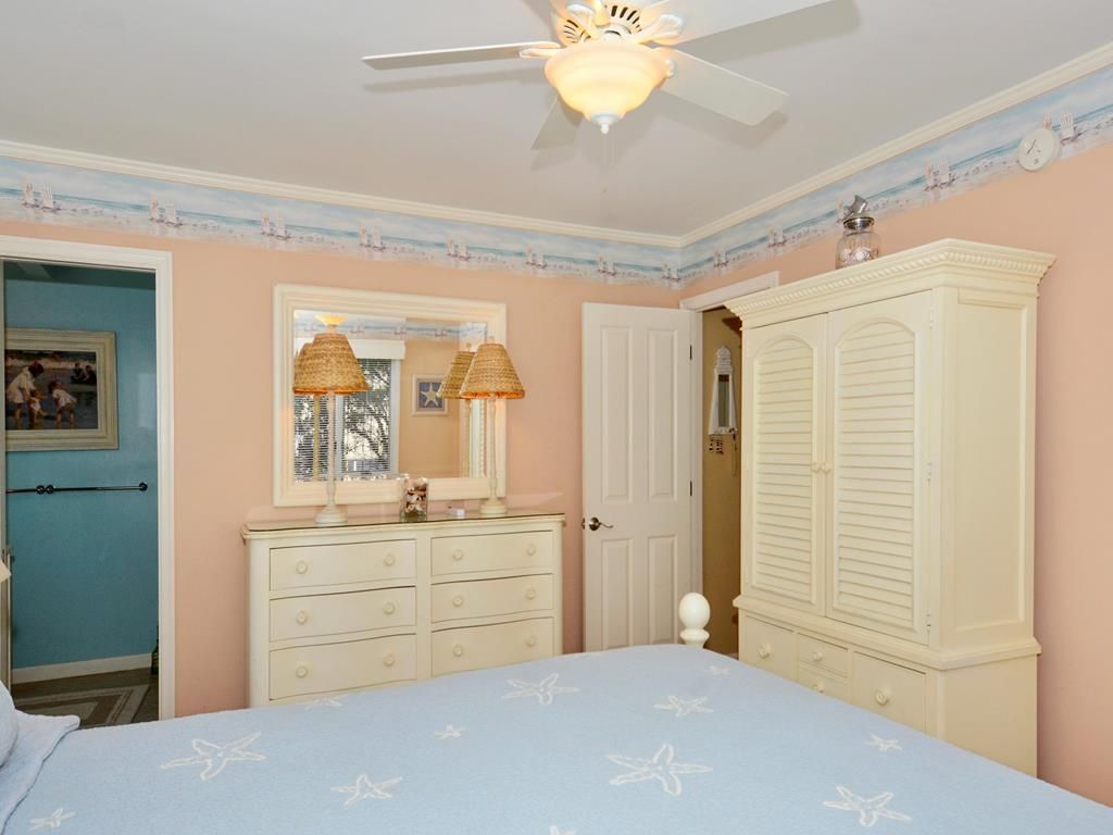 A bedroom with a bed, dresser, wardrobe, ceiling fan, and a door.