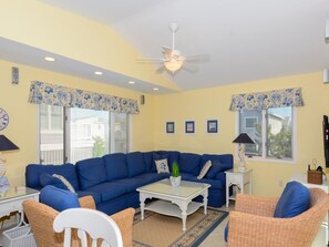 A living room with a blue sectional sofa, a white coffee table, wicker chairs, and a ceiling fan. - 4BR House w/ Deck | Close to Beach! (South Bethany Beach)