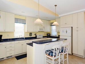 A kitchen with white cabinets, a central island with bar stools, a microwave, and a refrigerator. - 4BR House w/ Deck | Close to Beach! (South Bethany Beach)