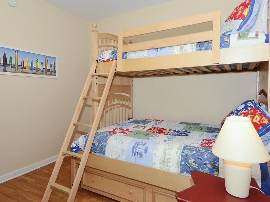 A bunk bed with a wooden ladder, a quilted bedspread, and a nightstand with a lamp.