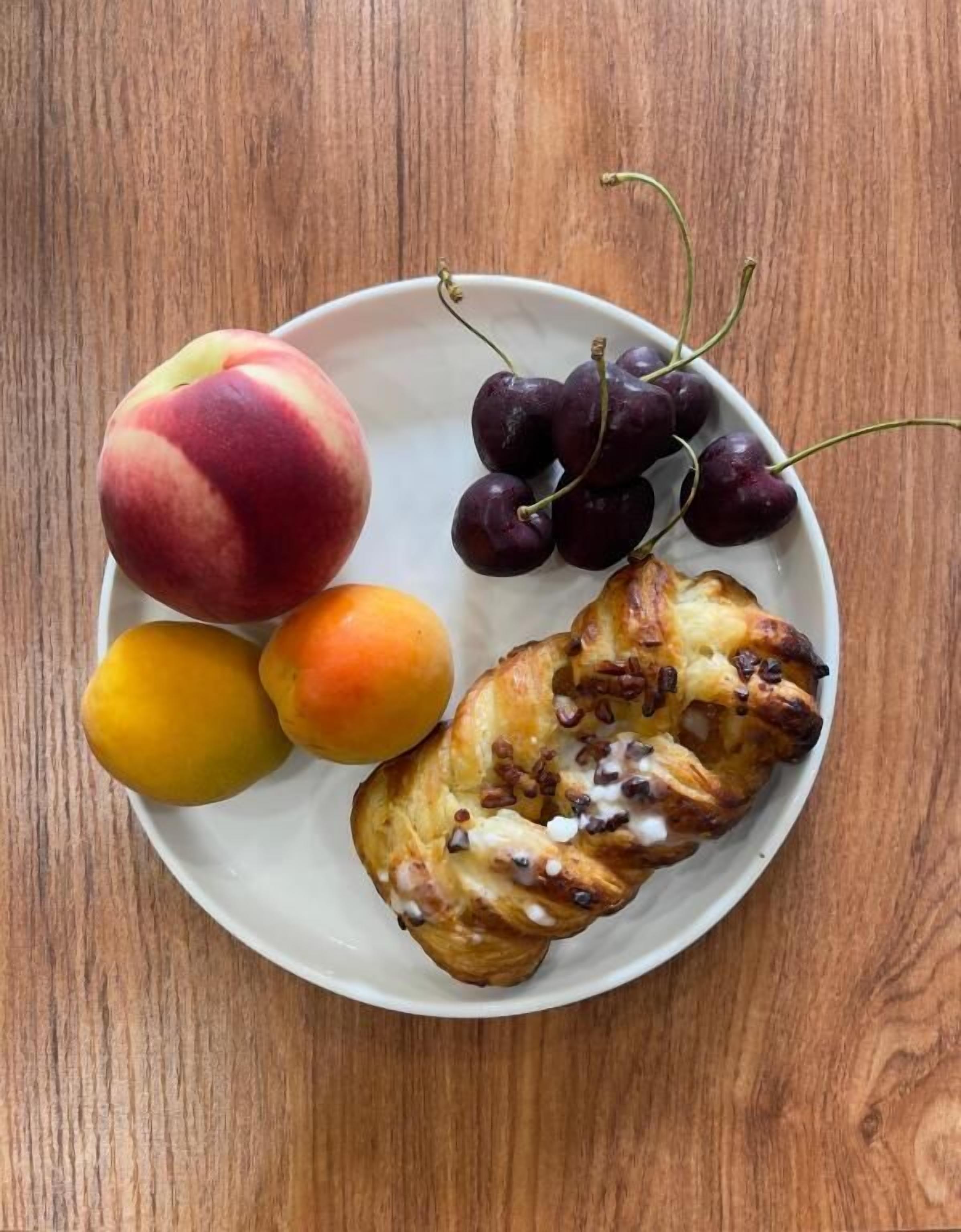 A plate with a pastry, peaches, and cherries on a wooden table.