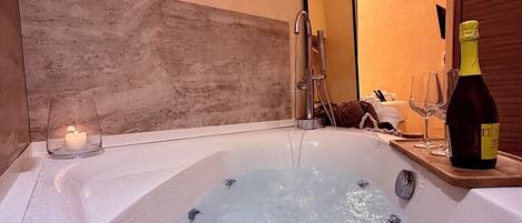 A hot tub with a candle and a bottle of champagne on a wooden tray.