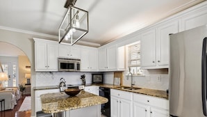 A modern kitchen with white cabinets, a granite countertop, a stainless steel refrigerator, and a bar stool area. - 3BR House near Bethany Beach | Pool Access (Frankford)