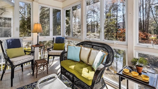 A sunroom with wicker furniture, large windows, and a view of trees. - 3BR House near Bethany Beach | Pool Access (Frankford)