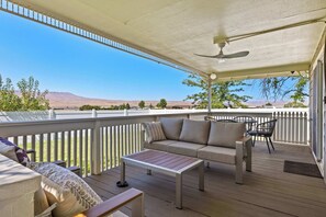 A covered outdoor seating area with a sofa, a table, and chairs, overlooking a landscape with trees and distant hills. - LlTTLE GEM on the GREEN - community pool (Desert Aire)