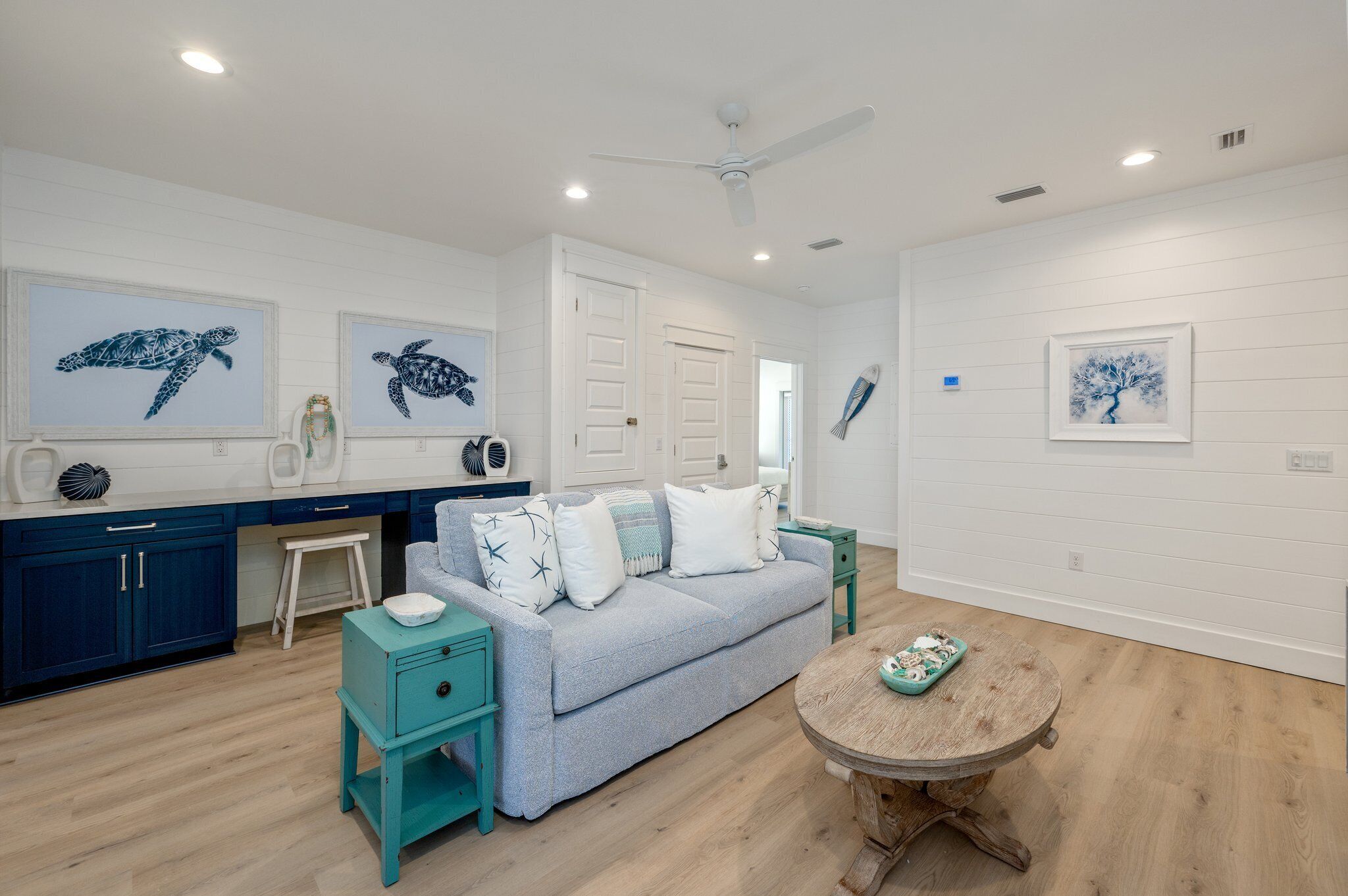A room with a light blue sofa, teal side tables, a wooden coffee table, and artwork of sea creatures.