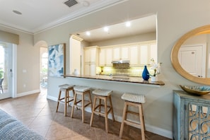 A kitchen with a bar area, wooden stools, and a large mirror. - Direct Beach Access Beautiful Resort Balcony (Holmes Beach)