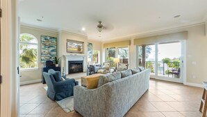 A spacious living room with a fireplace, a large sofa, a dining area, and a view through large windows. - Direct Beach Access Beautiful Resort Balcony (Holmes Beach)