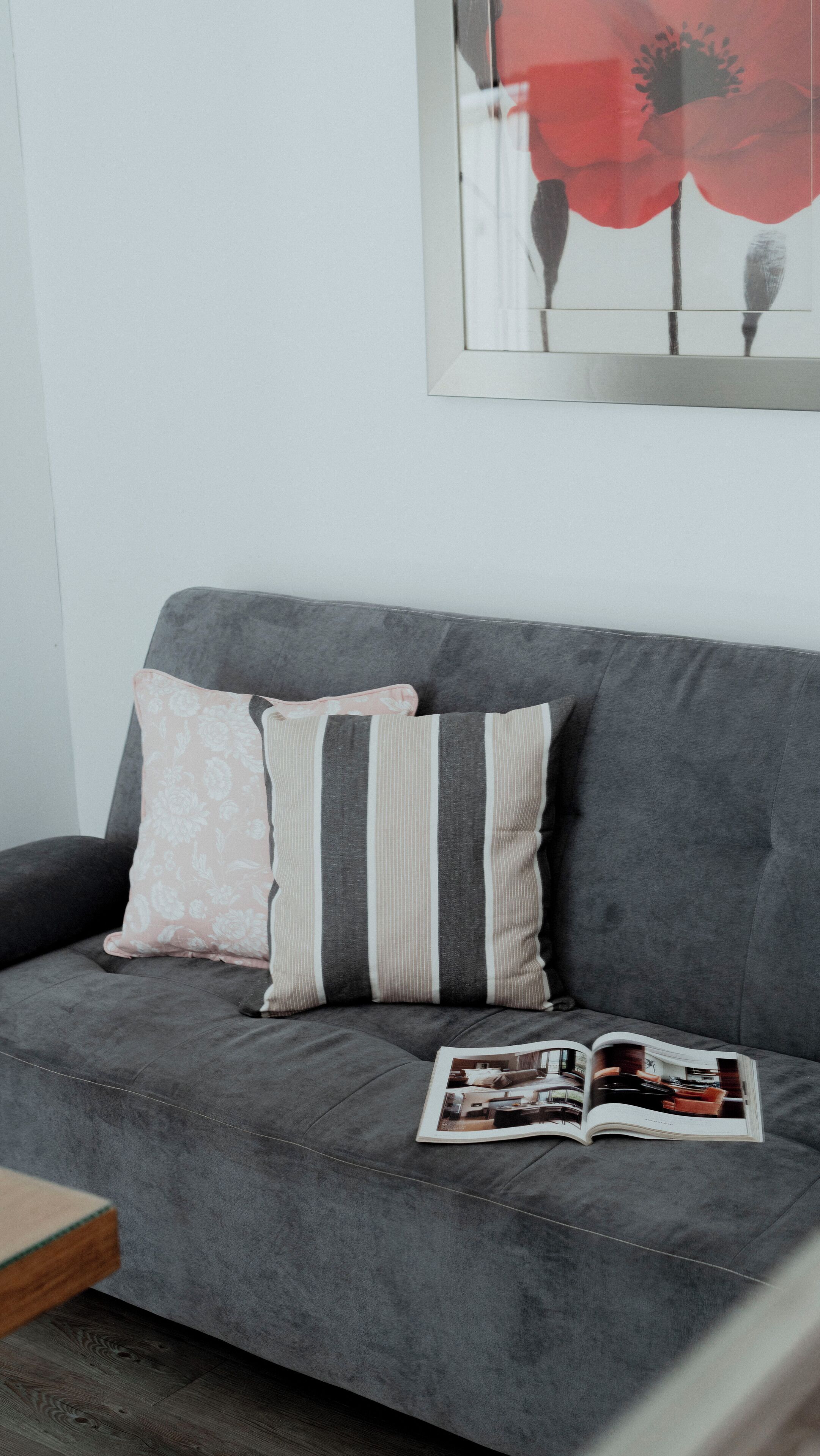 Un canapé gris agrémenté de coussins à rayures et à motifs floraux, un magazine posé dessus et une œuvre d’art encadrée au-dessus.