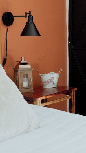 Une chambre à coucher avec une table de chevet en bois, un lit blanc, une lampe, une lanterne et un seau décoratif.