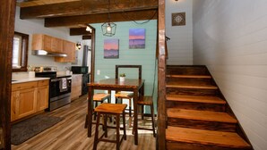 A rustic kitchen with wooden cabinets, a dining table with chairs, and a wooden staircase. - Charming 2-bedroom cottage in Homer perfect for relaxing stays. (Homer)