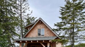 A cabin with a wooden deck, surrounded by tall grass and trees. - Charming 2-bedroom cottage in Homer perfect for relaxing stays. (Homer)