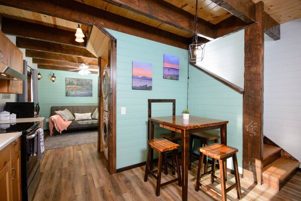 A cozy interior with a dining area, wooden beams, a sofa, and artwork on the walls.