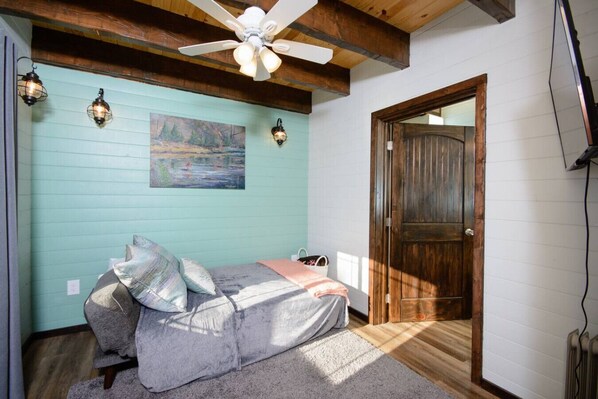 Un dormitorio con cama, ventilador de techo, un cuadro y una puerta de madera.