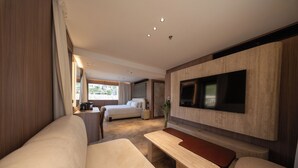 A modern hotel room with a large bed, a flat-screen TV mounted on the wall, a wooden bench, and a small table.