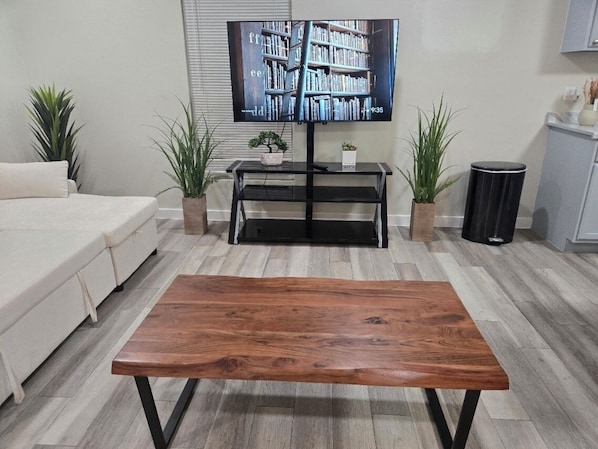 A living room with a wooden coffee table, a sofa, a TV on a stand, and potted plants.