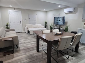 A modern living room with a wooden dining table, beige sofas, and a flat-screen TV.