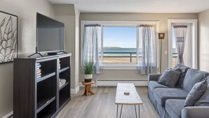Una sala de estar con televisor, estantería y vista a la playa.