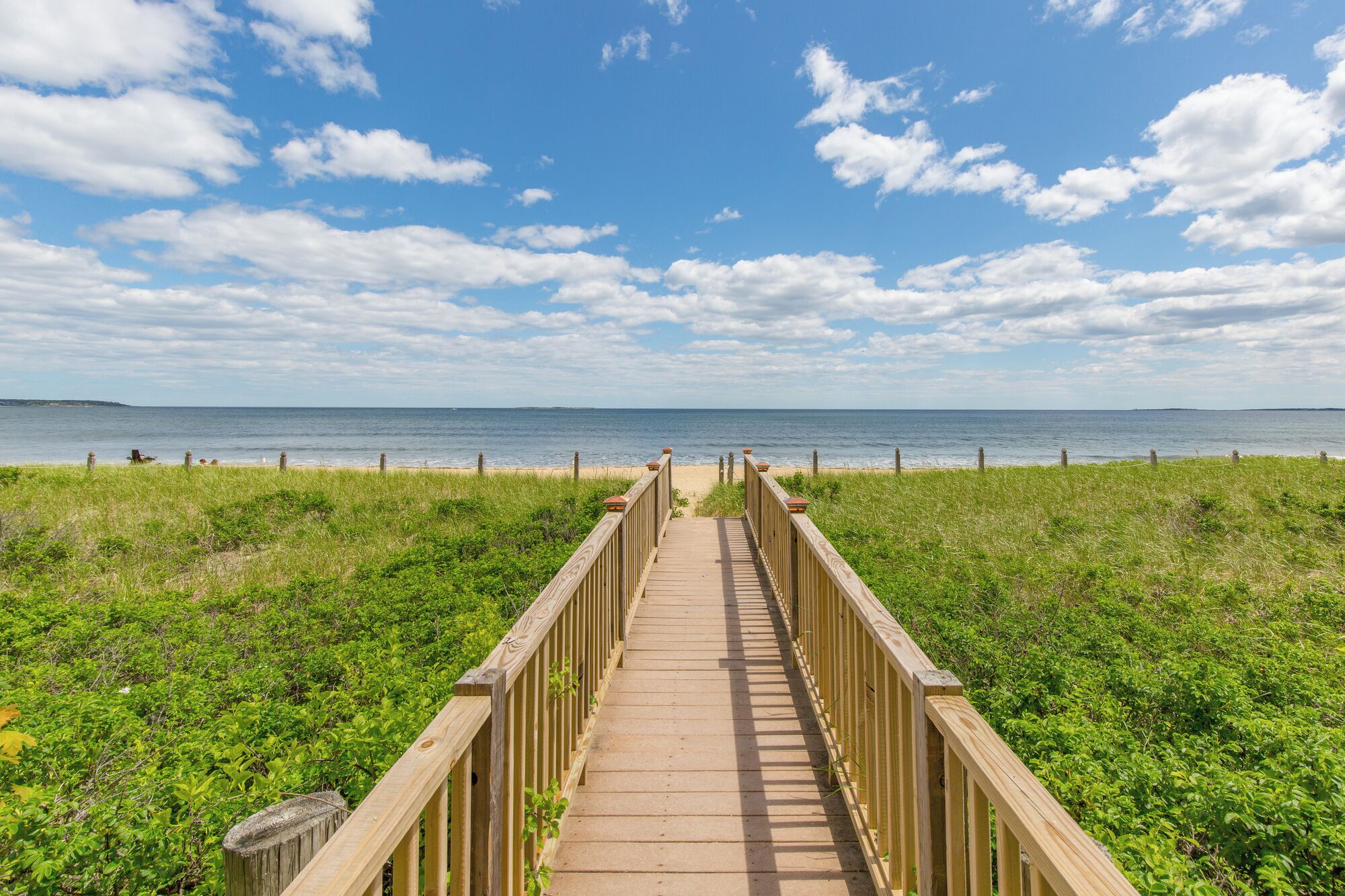 A wooden boardwalk leading to a beach with a clear sky and ocean view.