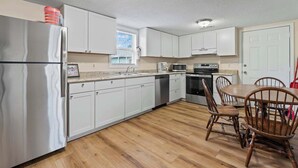 Una cocina moderna con armarios blancos, electrodomésticos de acero inoxidable y una mesa de comedor de madera con sillas.