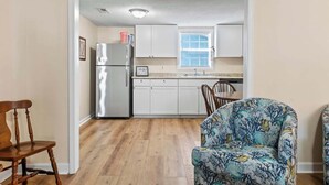 Una cocina con armarios blancos, un refrigerador de acero inoxidable y una ventana con persianas.