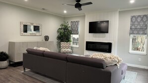Ein modernes Wohnzimmer mit einem Ecksofa, einem Flachbildfernseher, einem Deckenventilator und einem großen Fenster mit Blick.
