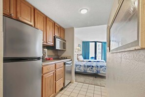A compact kitchen with wooden cabinets, a stainless steel refrigerator, and a microwave. - Carol's Coastal Getaway (Myrtle Beach)