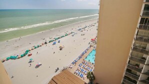 A beach view from a balcony with a pool area, beach umbrellas, and lounge chairs. - Carol's Coastal Getaway (Myrtle Beach)