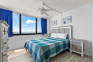 A bedroom with a bed, a nightstand, a dresser, a ceiling fan, and a window with curtains. - Sands Beach Club 2BR Ocean Front Condo 728 (Myrtle Beach)