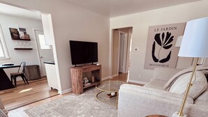 En moderne stue med et fladskærms-tv, en grå sofa, et træ sofabord og en stor måtte.