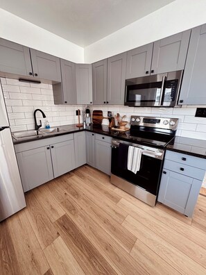 A modern kitchen with grey cabinets, a black countertop, a stainless steel oven, and a microwave.