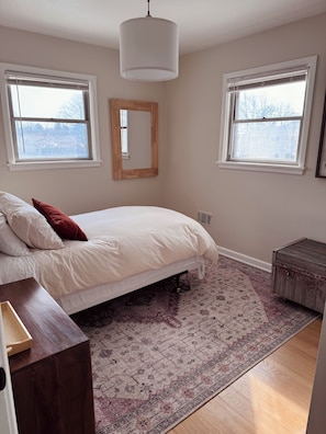 A bedroom with a bed, a wooden nightstand, a rug, and two windows.