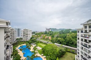 Un immeuble résidentiel de grande hauteur doté de nombreux balcons, d’un complexe de piscines et d’une végétation luxuriante.