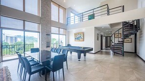 A spacious living area with a pool table, a dining table with chairs, and a staircase leading to an upper level. - 5 Bedroom Penthouse Ocean Views Jacobay 21002 (Jaco)