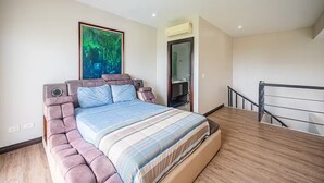 A bedroom with a large bed, a painting on the wall, and a bathroom visible through an open door. - 5 Bedroom Penthouse Ocean Views Jacobay 21002 (Jaco)