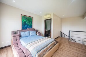 Une chambre à coucher avec un grand lit, un tableau accroché au mur et une salle de bain visible à travers une porte ouverte.