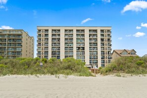 A multi-story hotel with balconies, located near a beach with sand and vegetation. - "The Salty Compass" 3 BR Ocean Front in Windy Hill (North Myrtle Beach)