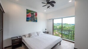 A bedroom with a large bed, a ceiling fan, a nightstand, a painting, and a balcony with a view. - 7 Bedroom Penthouse Ocean & Mountain Views JB31001 (Jaco)