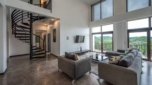 A spacious living area with a modern staircase, a flat-screen TV, and a balcony with a scenic view. - 7 Bedroom Penthouse Ocean & Mountain Views JB31001 (Jaco)