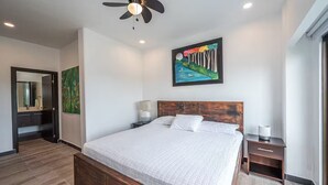 A modern bedroom with a large bed, a ceiling fan, a painting, and a nightstand with a lamp. - 7 Bedroom Penthouse Ocean & Mountain Views JB31001 (Jaco)