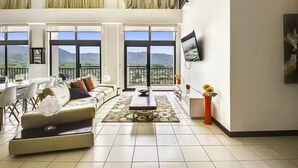 A spacious living room with a sofa, dining table, and chairs, large windows with a mountain view, and a flat-screen TV on the wall. - 7 Bedroom Penthouse Ocean & Mountain Views JB31002 (Jaco)