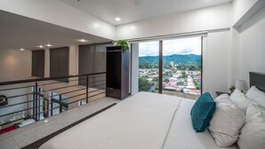 A modern hotel room with a large bed, a balcony with a city view, and a staircase leading to an upper floor. - 7 Bedroom Penthouse Ocean & Mountain Views JB31002 (Jaco)