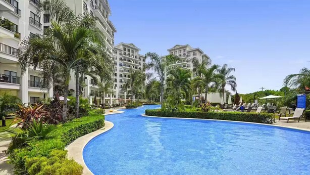 A swimming pool surrounded by lush greenery and palm trees, with a multi-story building in the background. - 7 Bedroom Penthouse Ocean & Mountain Views JB31002 (Jaco)