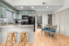 A modern kitchen with a central island, wooden stools, and a dining area with a table and chairs. - Anchors Away Two Blocks to Surfside Beach. (Surfside Beach)