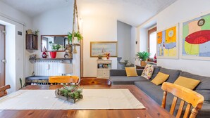 A cozy living room with a wooden dining table, a gray sofa with yellow cushions, and a bookshelf. - Casa Olinda, which opens to Mount Emilius and the Gran Paradiso massif. (Saint-Christopher)