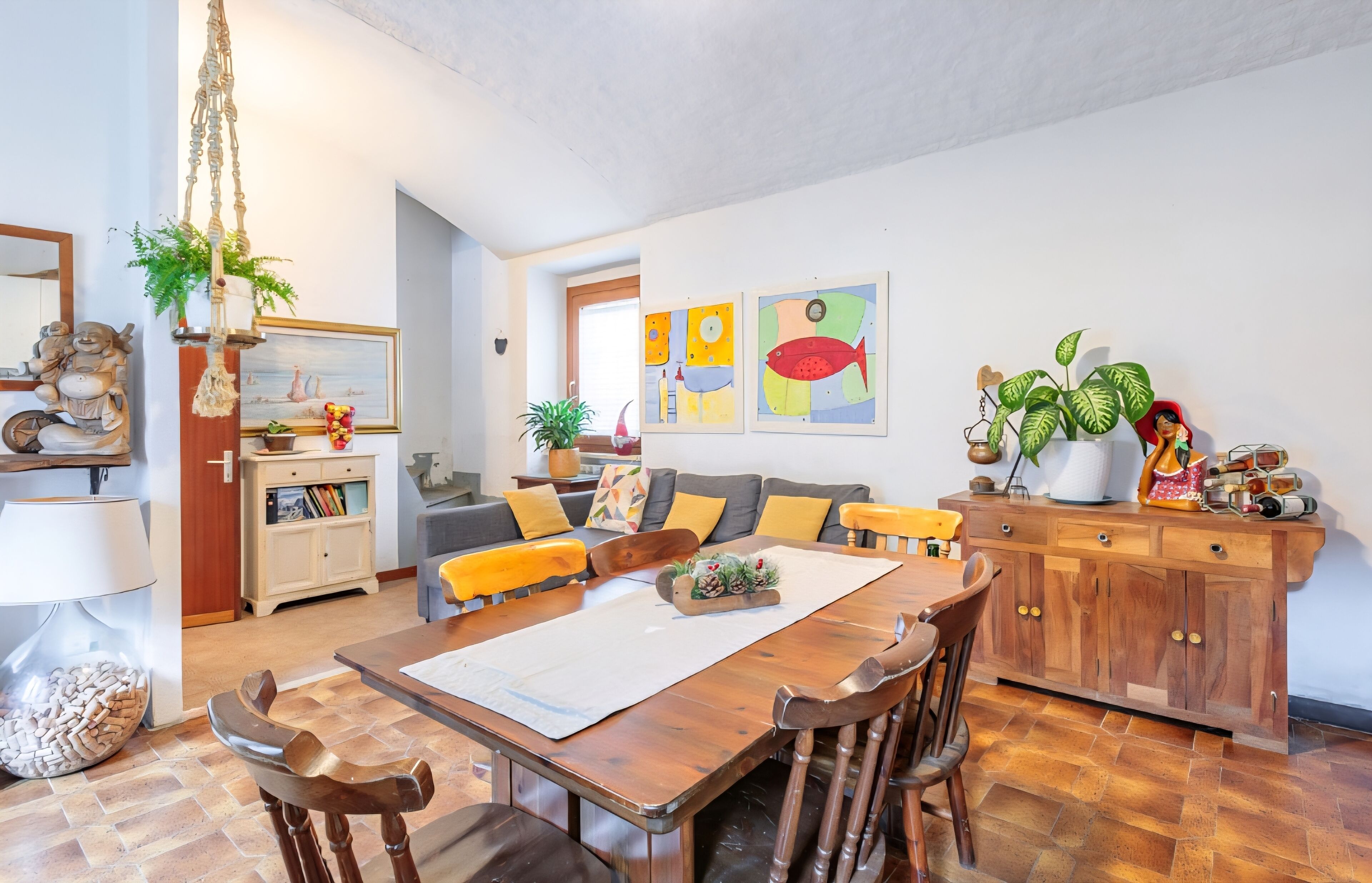 Una sala acogedora con una mesa de madera para comer, asientos cómodos, un sofá con cojines y una estantería.