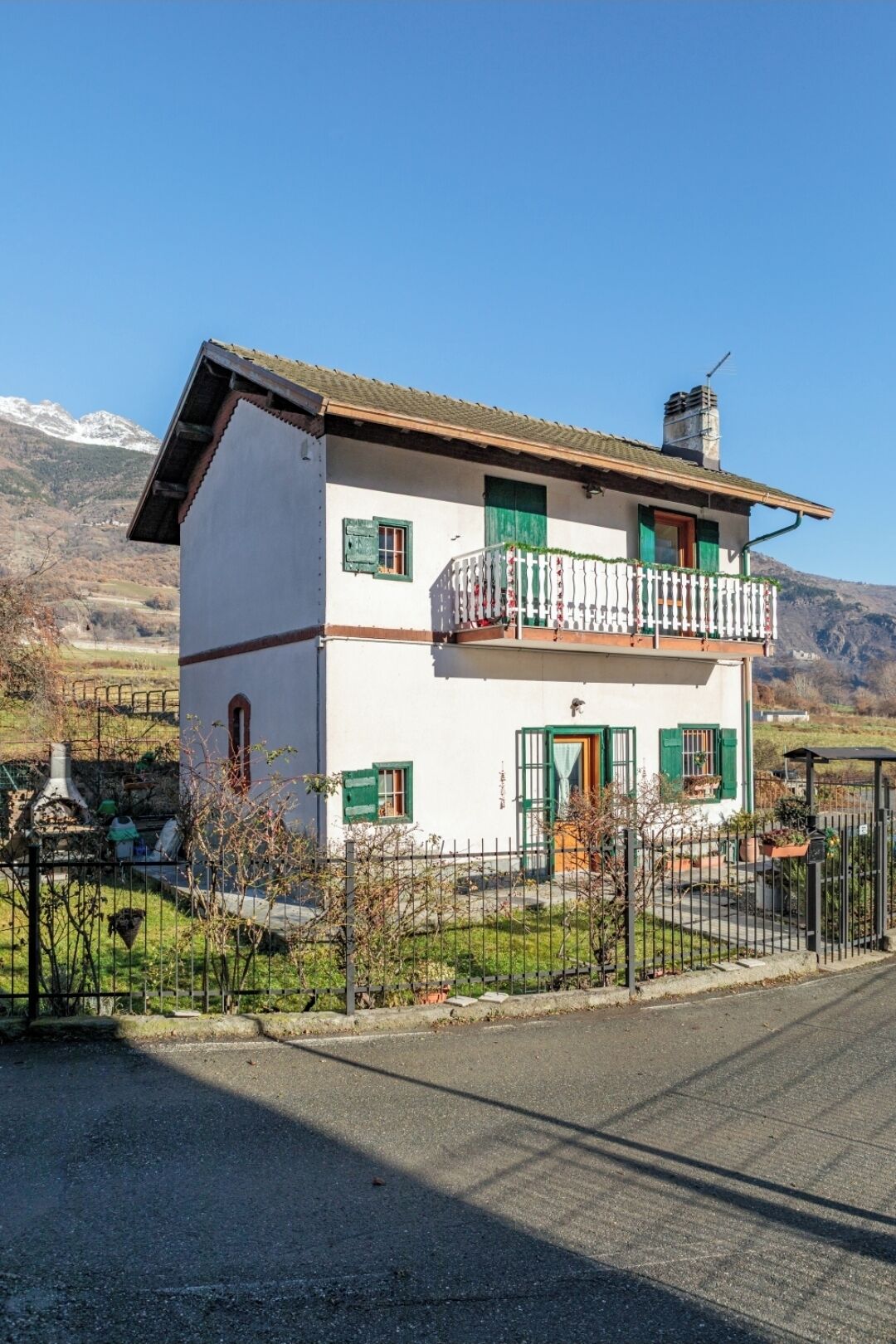 Una casa a due piani con un balcone, una ciminiera e lo sfondo di una montagna.