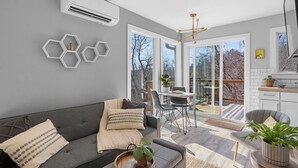A modern living room with a grey sofa, a dining area with a table and chairs, and a kitchen area with cabinets and a countertop. - Bright and Tranquil Guesthouse! (Woodfin)