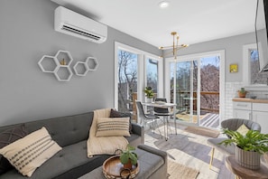 Ein modernes Wohnzimmer mit grauem Sofa, einem Essbereich mit Tisch und Stühlen sowie einer Küchenzeile mit Schränken und Arbeitsplatte.