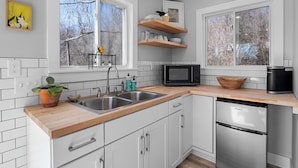 A modern kitchen with white cabinets, a wooden countertop, a built-in microwave, and a stainless steel refrigerator. - Bright and Tranquil Guesthouse! (Woodfin)